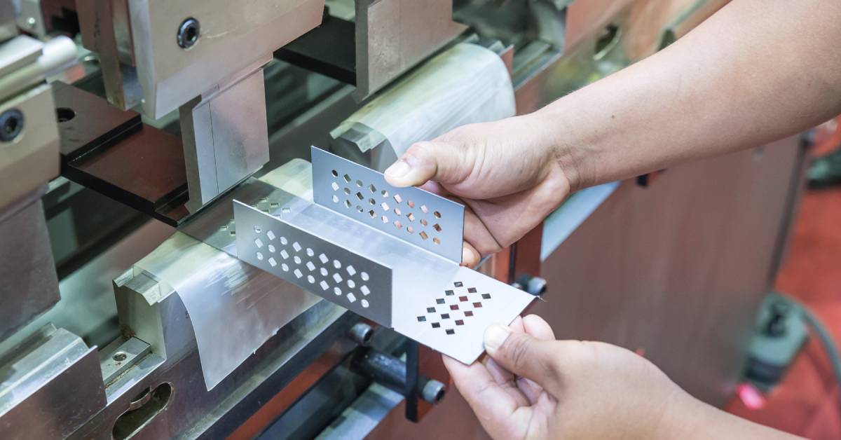 A gloveless worker removing a folded piece of perforated metal from a folding machine in an industrial facility.