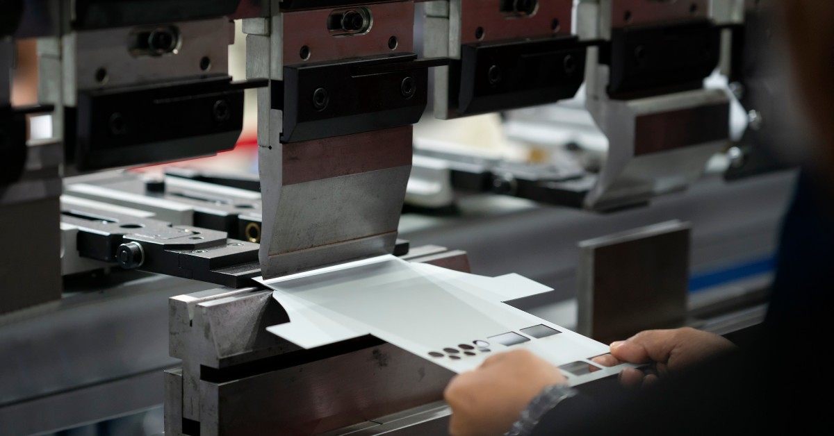 An operator holding a sheet of metal near a sheet bending machine. The metal has already been stamped.