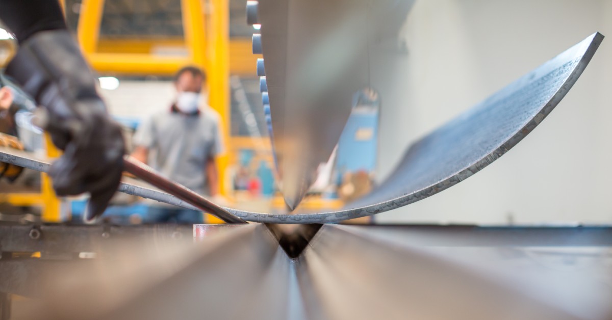 A worker using a pry bar to release a piece of metal from a metal bending machine in a metalworking shop.