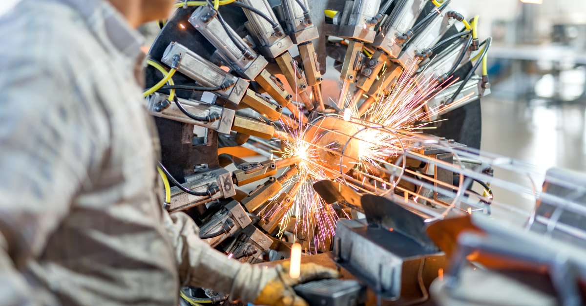 An electrical resistance welding machine. The machine operator is wearing a button-down shirt and heavy work gloves.