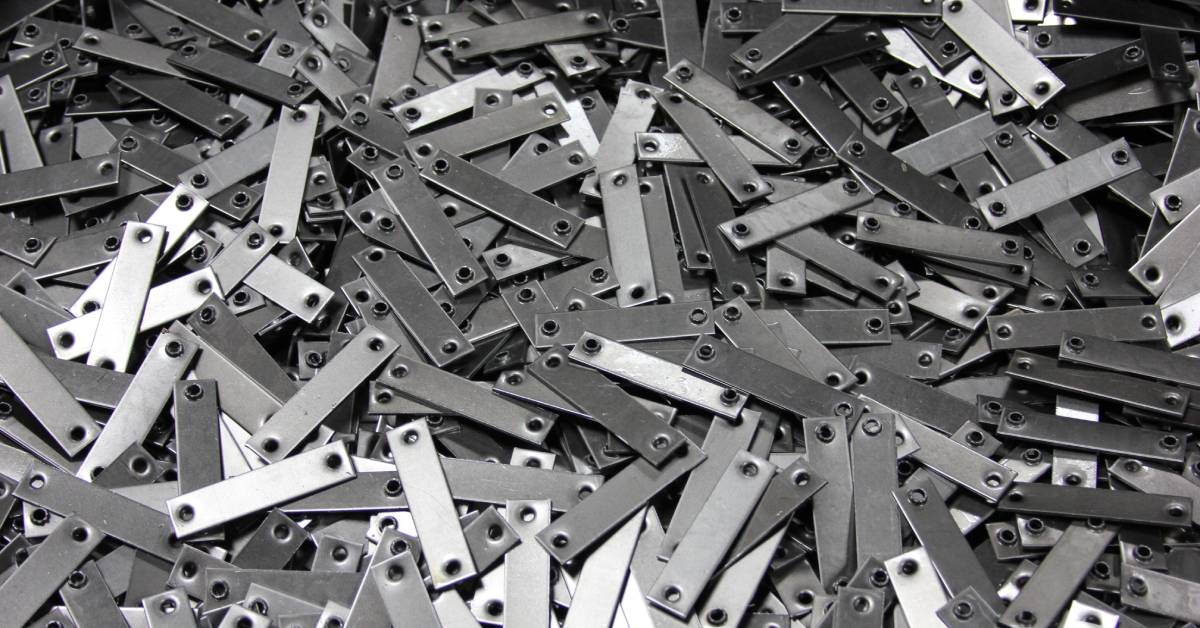 A large pile of steel pieces, each with a hole on either end. The holes have been punched through by a metal stamping machine.