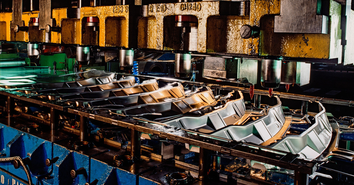 An industrial press machine with multiple pieces of stainless steel moving along underneath after being stamped.