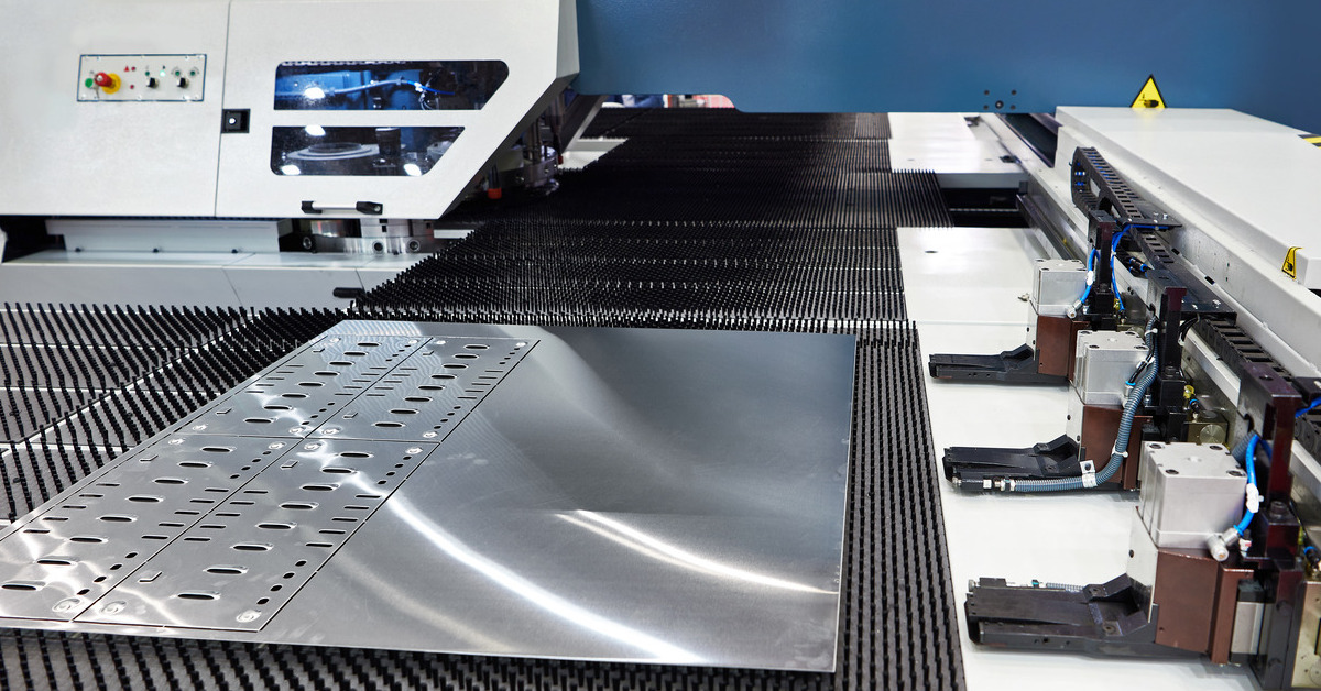 A turret press machine with a sheet of stainless steel on the punch surface. There are several holes punched out of the metal.
