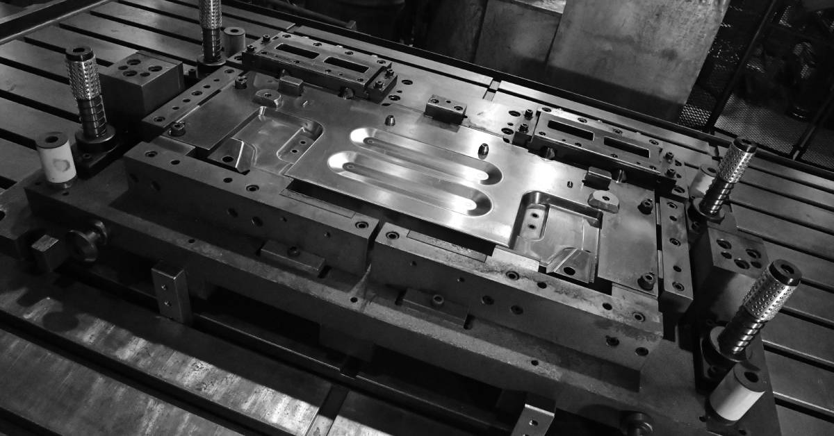 A sheet metal stamping tool die for automotive precision parts, pictured in black and white in a manufacturing facility.