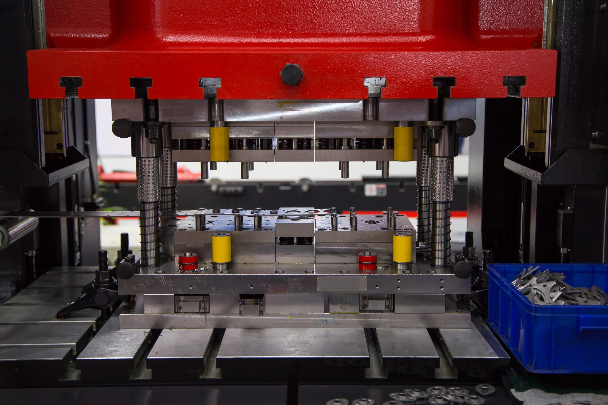Close-up of an industrial stamping machine used for precision metal forming. It features a red upper section and various mechanical components.