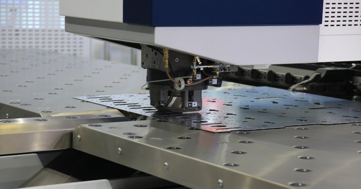 A CNC punching machine being used on a thin sheet of metal in an industrial manufacturing facility.