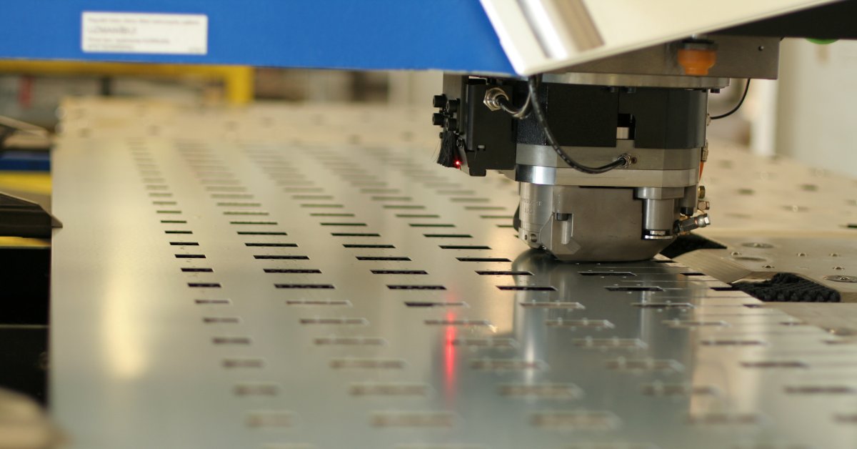 An industrial CNC punching machine is in the process of cutting out square shapes from a metal plate.