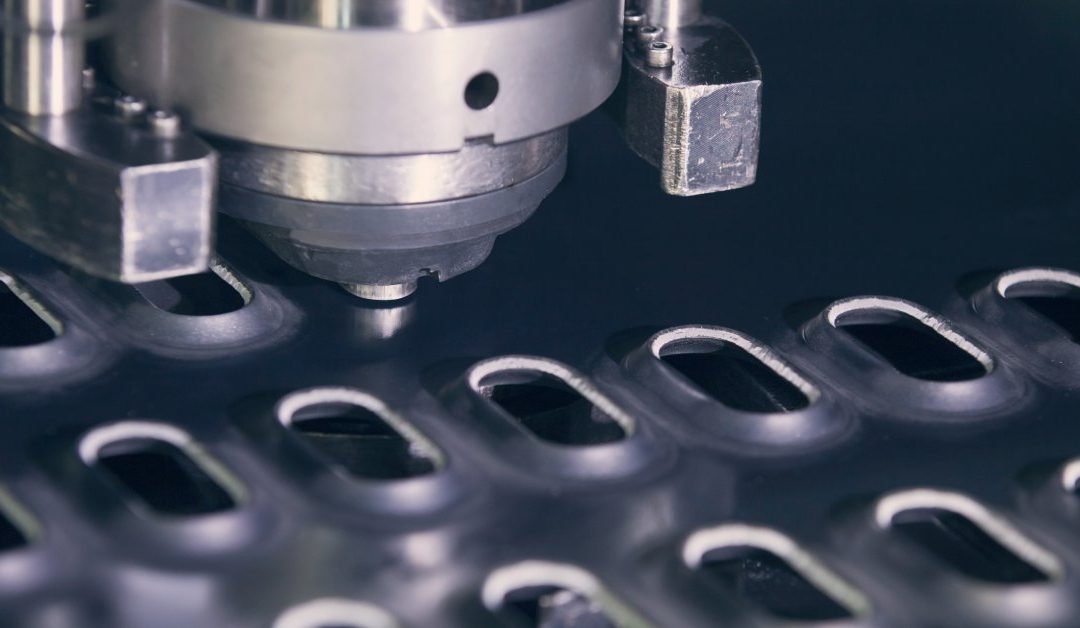 An industrial rotation CNC punching machine is creating many ovals in dark grey steel sheet metal.