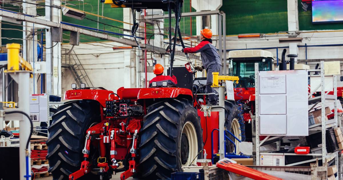 Industrial workers assembling a tractor trailer for agricultural applications in a large manufacturing facility.