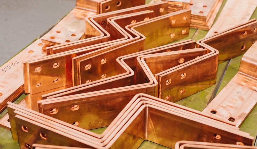 An assortment of brass busbars lay on a flat surface, with some in a bent shape while others are flat and rectangular.