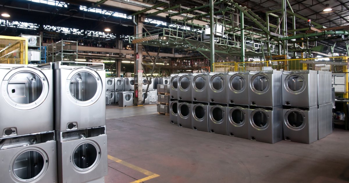 Numerous front-load washer and dryer machines organized next to one another inside of a large industrial warehouse.